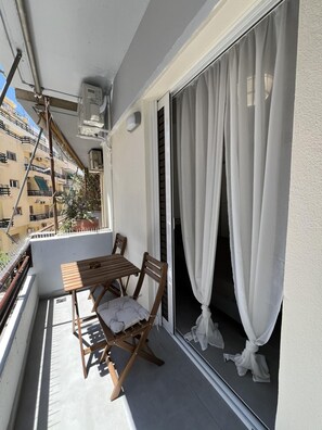 A balcony with a wooden table and chairs, a potted plant, and a view of a building. - Loutraki Haven 1 Bdrm 3 min to Beach (Loutraki-Agioi Theodoroi)