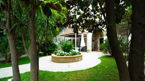 Un espace jardin agrémenté d’un bac à fleurs en pierre, d’un sentier et d’un bâtiment avec un toit en tuiles en arrière-plan.