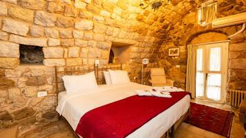 A bedroom with a stone wall, a bed with white bedding, a red throw blanket, and a wooden chair.