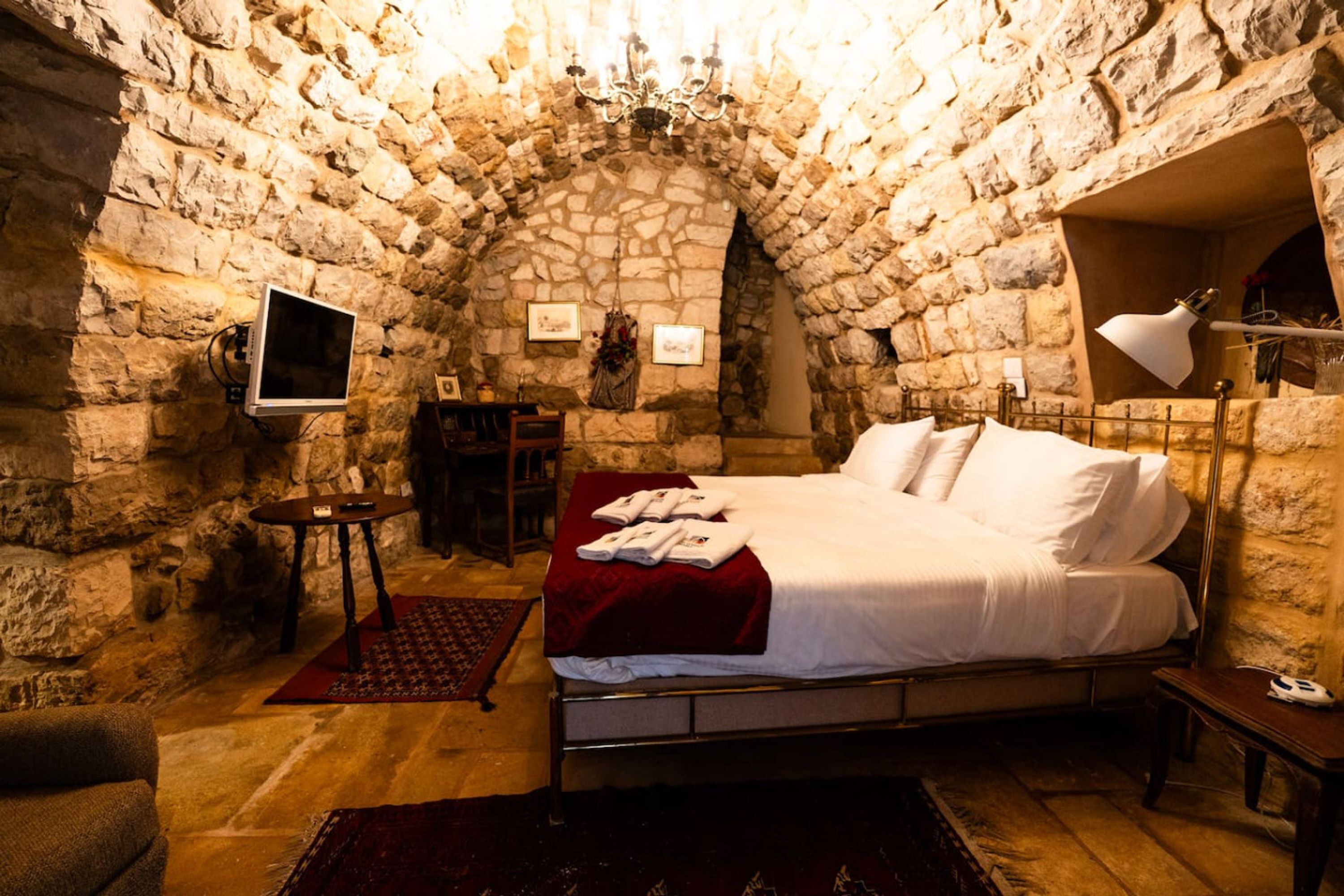 A stone-walled bedroom with a bed, a desk, and a television.