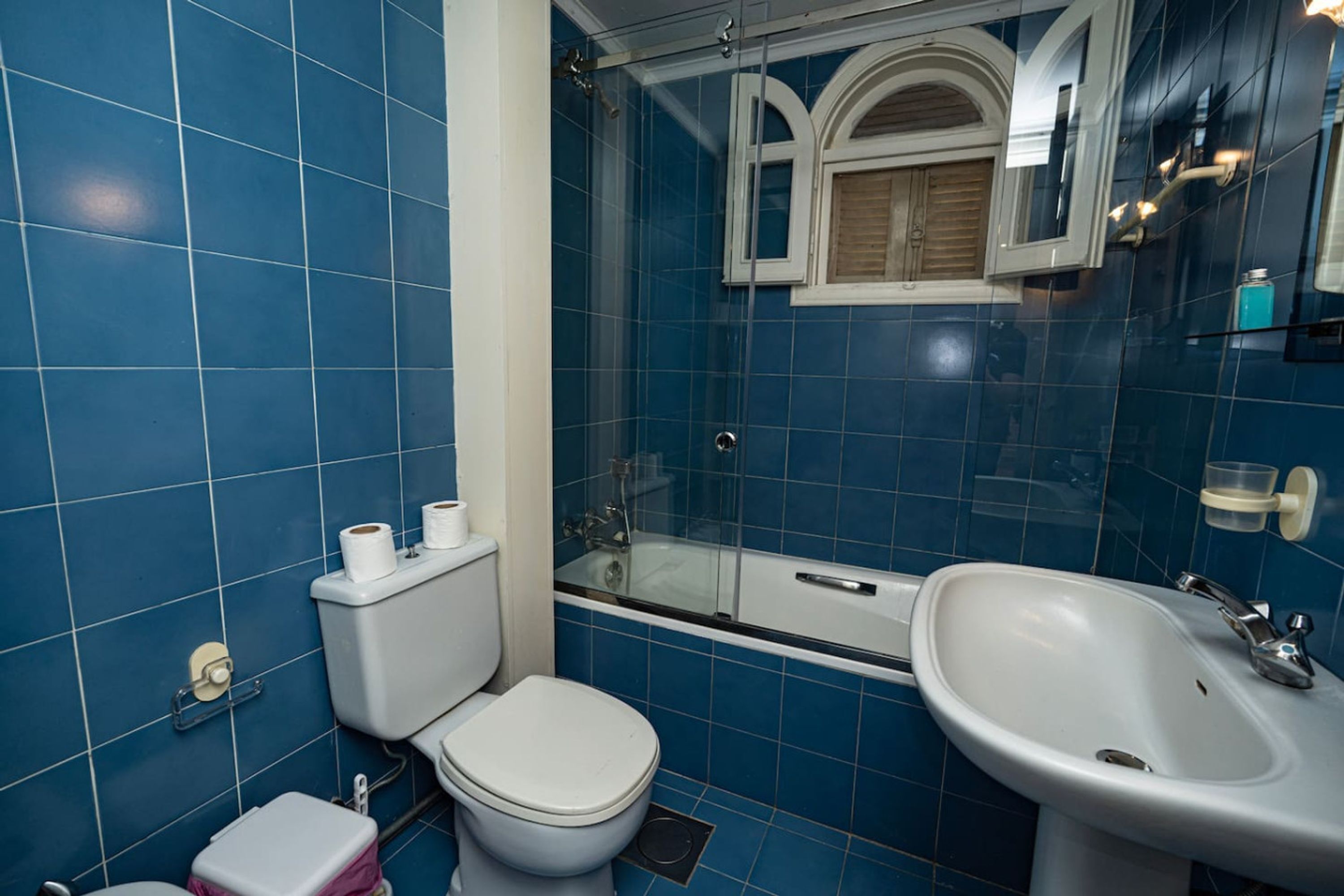 A bathroom with blue tiles, a toilet, a sink, and a glass-enclosed shower.
