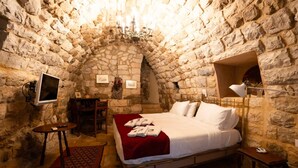 Une chambre aux murs de pierre, avec un lit, une table de chevet, une lampe et un petit bureau avec une chaise.