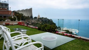Une terrasse sur le toit, avec des chaises blanches, une table en verre et une vue sur le paysage urbain de la côte.