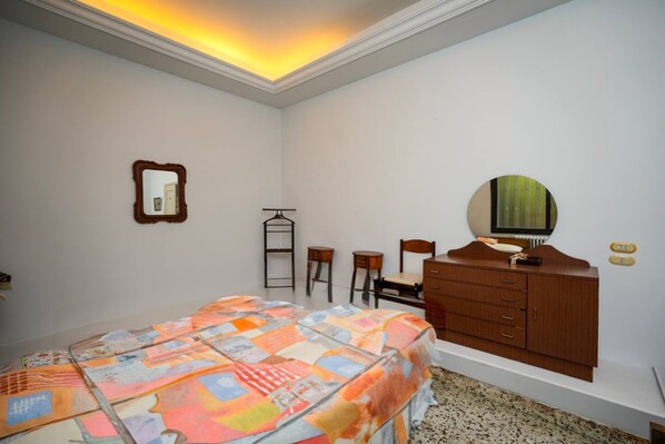 Un dormitorio con cama, cómoda, espejo, silla y una mesita.