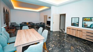 A modern living room with a wooden dining table, grey upholstered chairs, a black and white marble floor, and a built-in TV. - The Ajaltoun Villa in Ajaltoun (Ajaltoun)