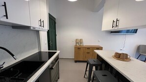 Et moderne køkken med en sort komfur, hvide skabe og et træskab med en grøn dør. Der er to barstole og et bord med en bakke kopper.