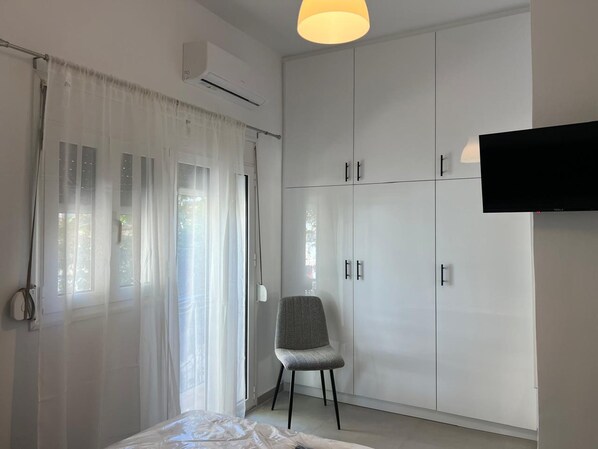 A bedroom with a bed, a chair, a wardrobe, and a TV. - Loutraki s Seaside Serenity 2 Bdrm (Loutraki-Agioi Theodoroi)
