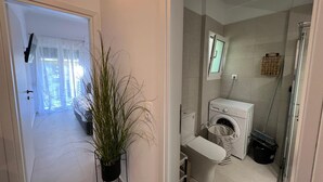Et lille badeværelse med vaskemaskine, toilet og bruseområde.