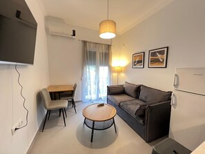A compact living space with a sofa, a dining table, a small round table, a TV, and a refrigerator. - Loutraki s Seaside Serenity 2 Bdrm (Loutraki-Agioi Theodoroi)