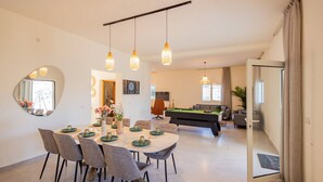 Ein modernes Wohnzimmer mit Billardtisch, Essbereich mit rundem Tisch und Stühlen sowie einem großen Spiegel an der Wand.