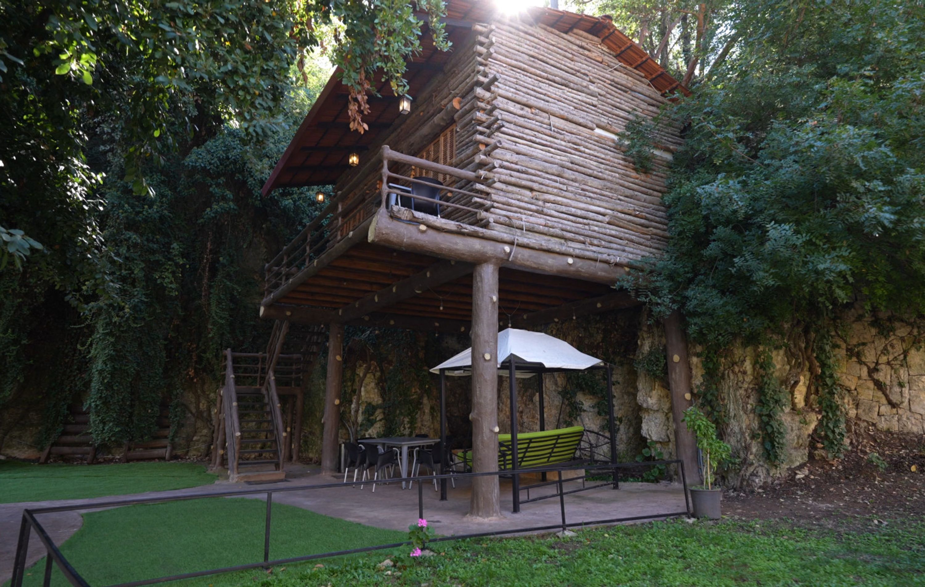 A rustic wooden cabin with a balcony, surrounded by lush greenery.