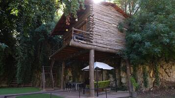 A rustic wooden cabin with a balcony, surrounded by lush greenery.