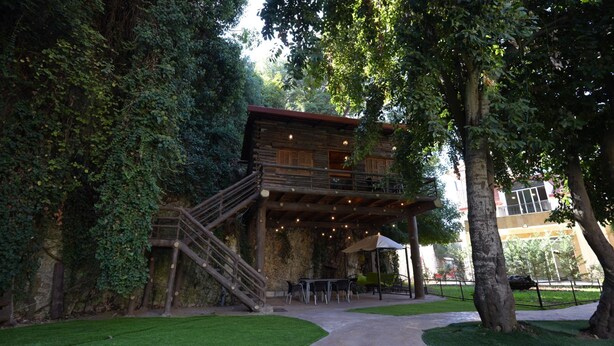 A rustic wooden cabin with a balcony and outdoor seating area surrounded by lush greenery.