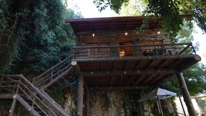 A rustic wooden cabin with a balcony, surrounded by dense foliage.