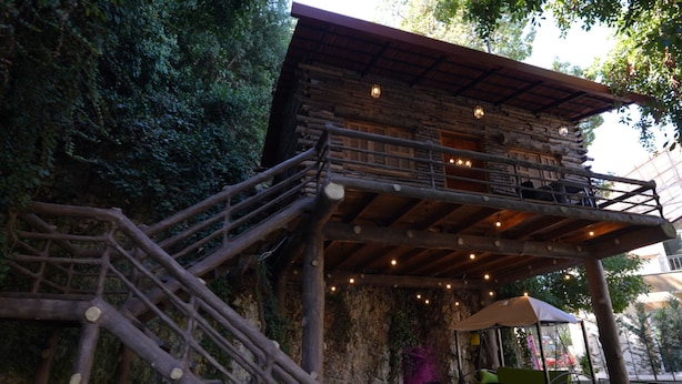 A rustic wooden building with a balcony, outdoor seating, and a stone wall. - Keserwan s Hillside Resort and Venue (Aazra Wil Aazr)