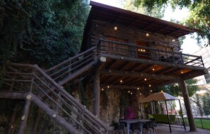 A rustic wooden building with a balcony, outdoor seating, and a stone wall. - Keserwan s Hillside Resort and Venue (Aazra Wil Aazr)