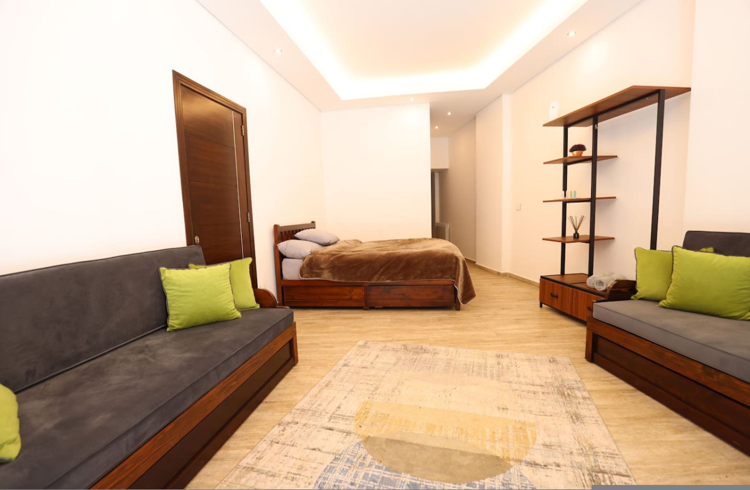A modern bedroom with a large bed, two sofas, a wooden wardrobe, and a ceiling light.