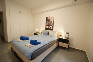 Ett modernt hotellrum med en stor säng, två sängbord, en garderob och en affisch med en stadsbild på väggen.