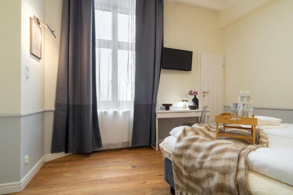A hotel room with a bed, a desk, a TV mounted on the wall, and a window with curtains.