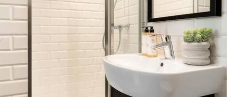 Un baño moderno con ducha envuelta en vidrio, lavamanos blanco con mueble negro y un espejo sobre el lavamanos.