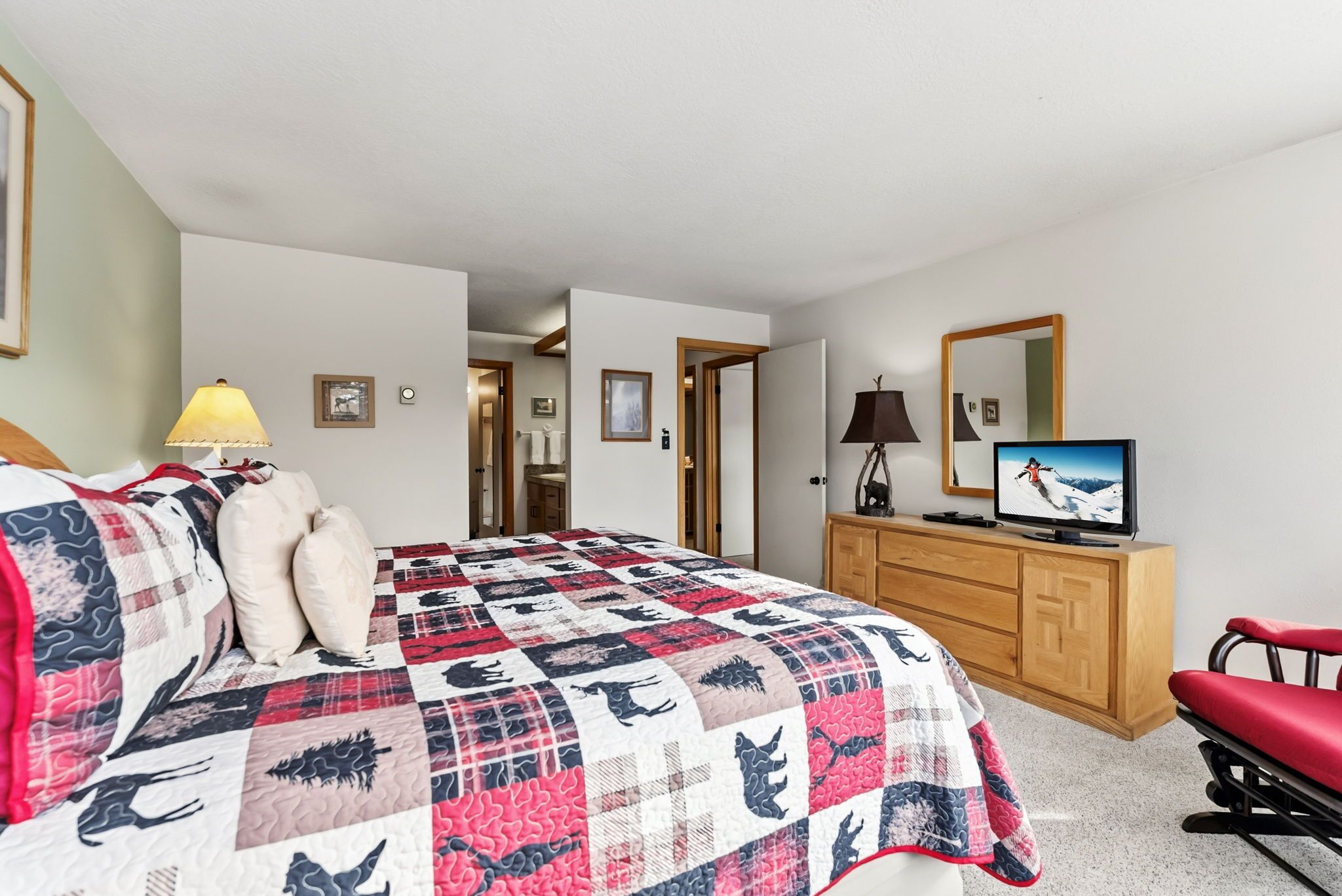 A bedroom with a large bed, a television, a dresser, and a red chair.