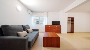 Una sala moderna con un sofá gris, una mesa de centro de madera y un televisor sobre un mueble de madera.