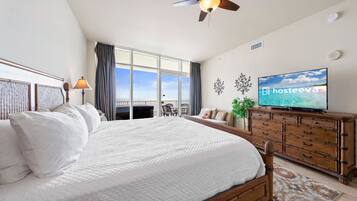 A spacious bedroom with a large bed, a ceiling fan, a television, and a balcony with a view.