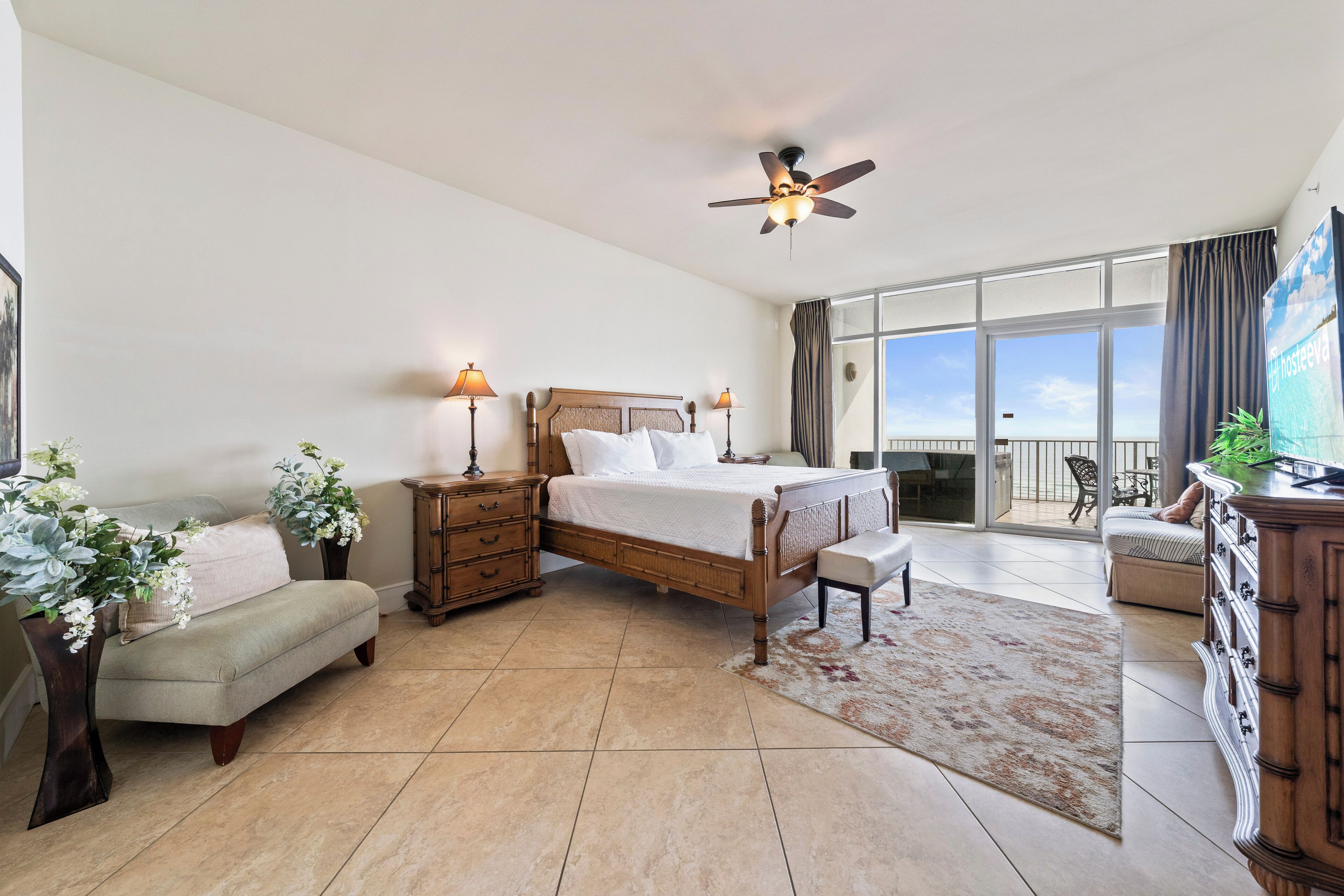A spacious bedroom with a large bed, a ceiling fan, and a view of the outdoors through a sliding glass door.