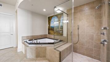 A modern bathroom with a glass-enclosed shower, a freestanding bathtub, and a large mirror reflecting a scenic painting.