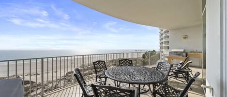 A balcony with a round table and chairs, overlooking a beach.