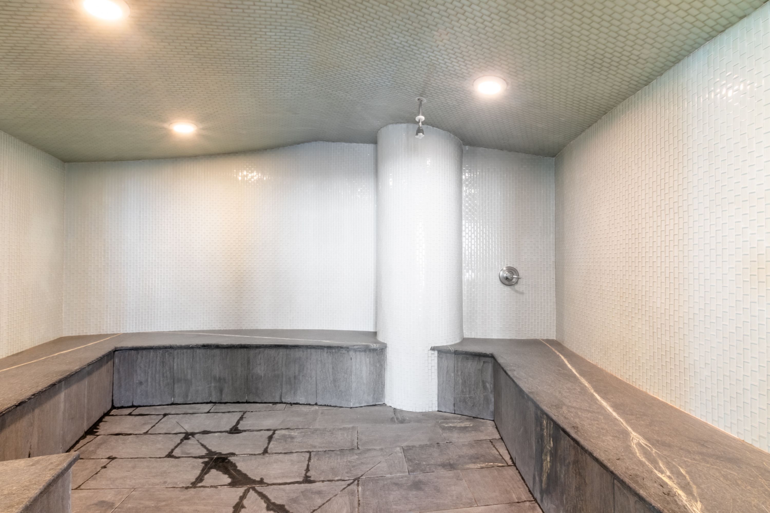 Un baño de vapor con piso de piedra, paredes de azulejos blancos y una columna central.