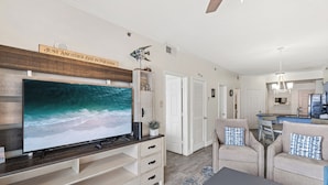 Un salon doté d’un grand téléviseur à écran plat, d’un meuble de rangement en bois, de deux fauteuils beiges et d’une table basse.
