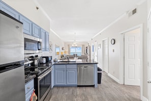 A modern kitchen with a central island, stainless steel appliances, and light blue cabinetry. - Tradewinds 1205 by Liquid Life (Orange Beach)