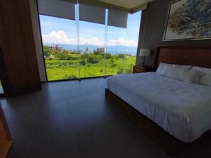 Slaapkamer met een groot bed, nachtkastje en uitzicht op een groen landschap door een glazen deur.
