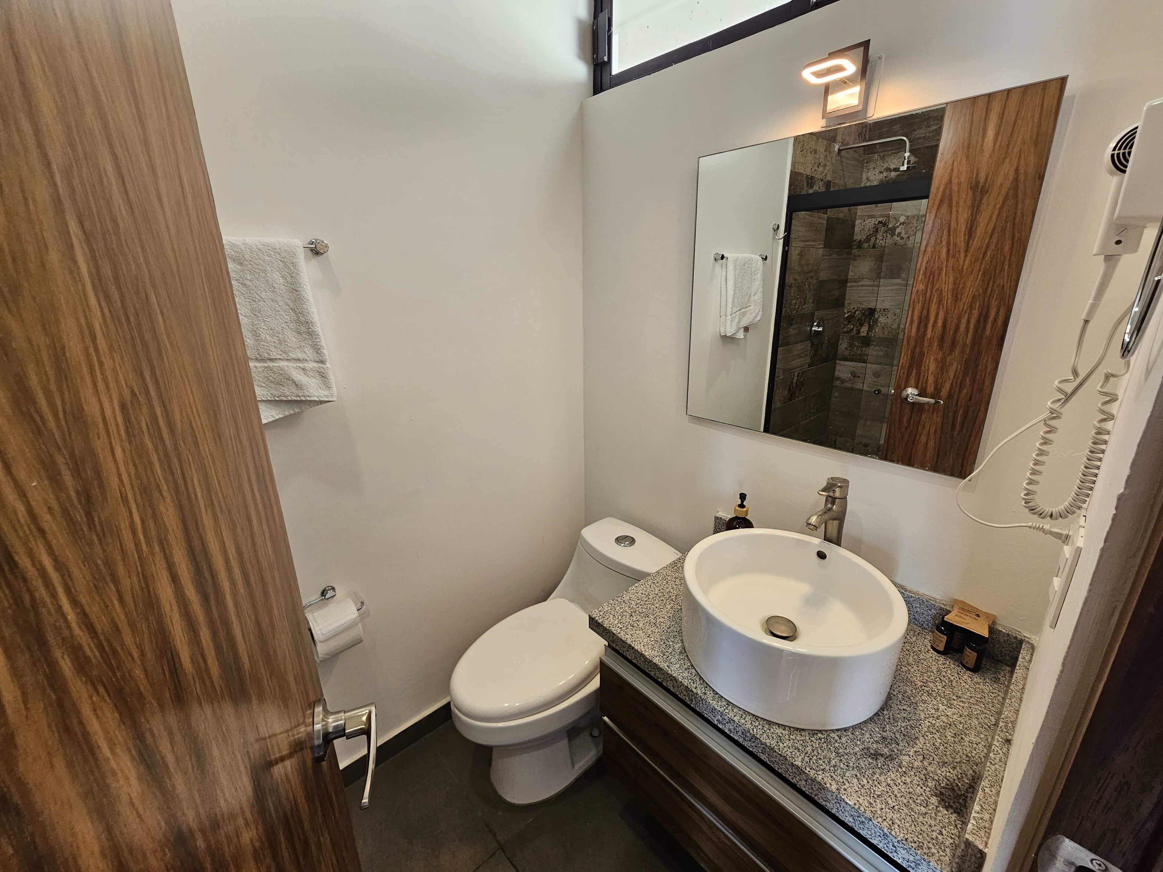 Un baño pequeño con inodoro blanco, lavamanos con espejo y zona de ducha con puerta de cristal.