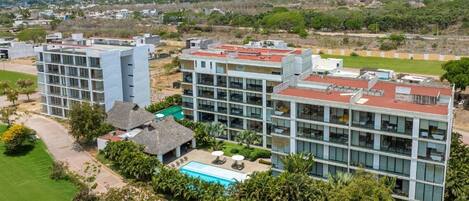 A modern hotel with multiple buildings, a swimming pool, and lush greenery.