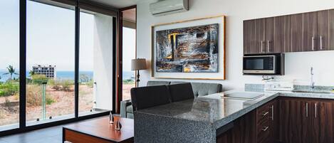 A modern kitchen with a large island, dark wood cabinets, and a view of the beach.