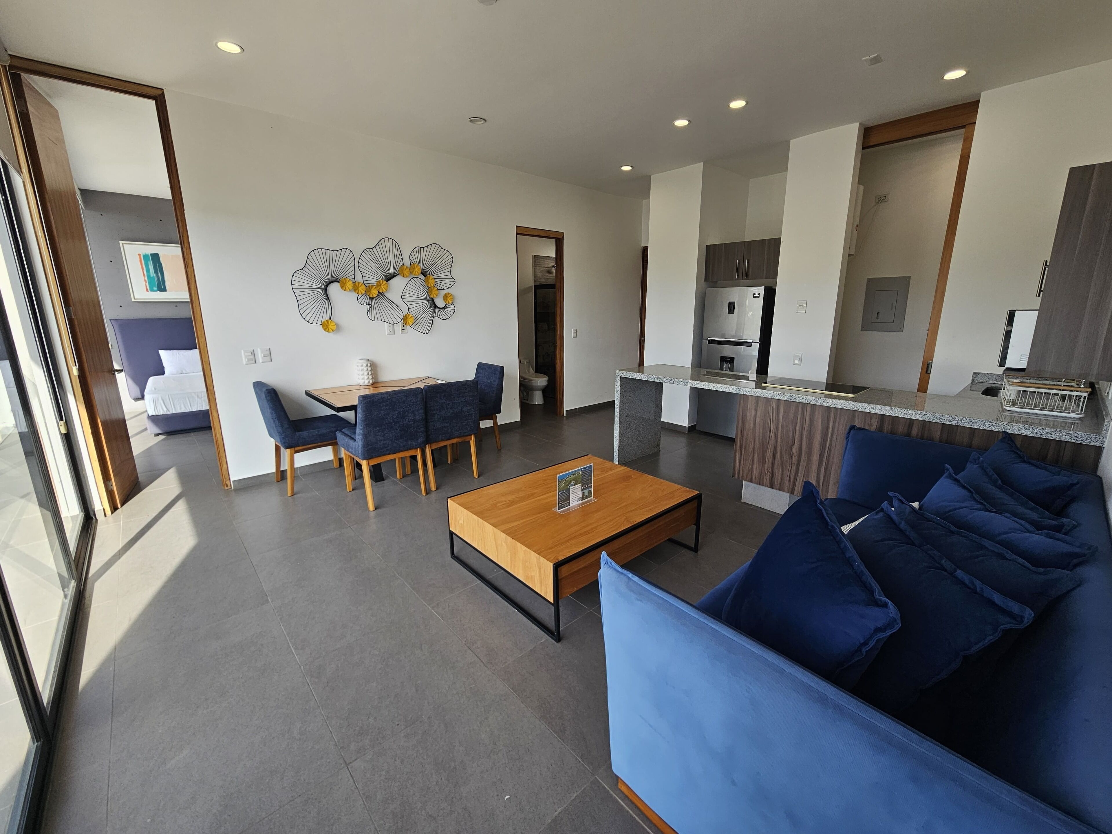 Una sala moderna con un sofá azul, una mesa de centro de madera y un comedor con sillas azules.