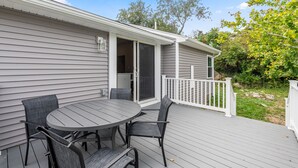 A deck with a round table and four chairs, a sliding glass door, and a white fence. - Beach Bound - Cape Ann Coastal Escape (Gloucester)