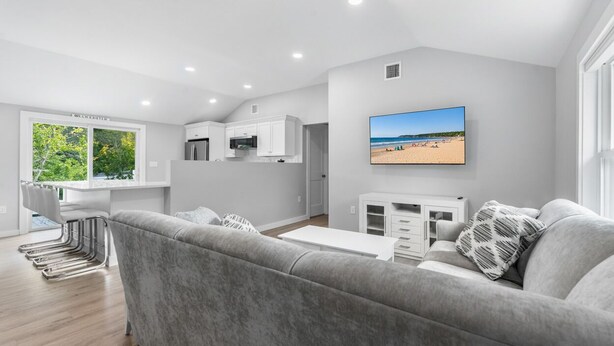 A modern living room with a grey sofa, a flat-screen TV, and a beach view. - Beach Bound - Cape Ann Coastal Escape (Gloucester)