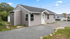 A single-story house with a gabled roof, a front porch, and a gravel driveway. - Beach Bound - Cape Ann Coastal Escape (Gloucester)