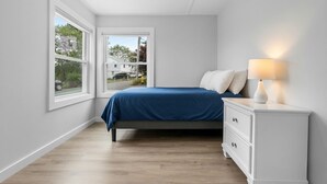 A bedroom with a bed, a nightstand, and a window. - Beach Bound - Cape Ann Coastal Escape (Gloucester)