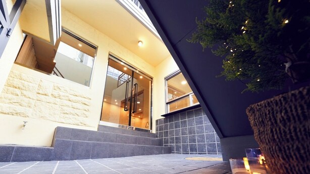 Una entrada moderna de edificio con fachada de piedra, puertas de cristal y una escalera que conduce a un nivel superior.