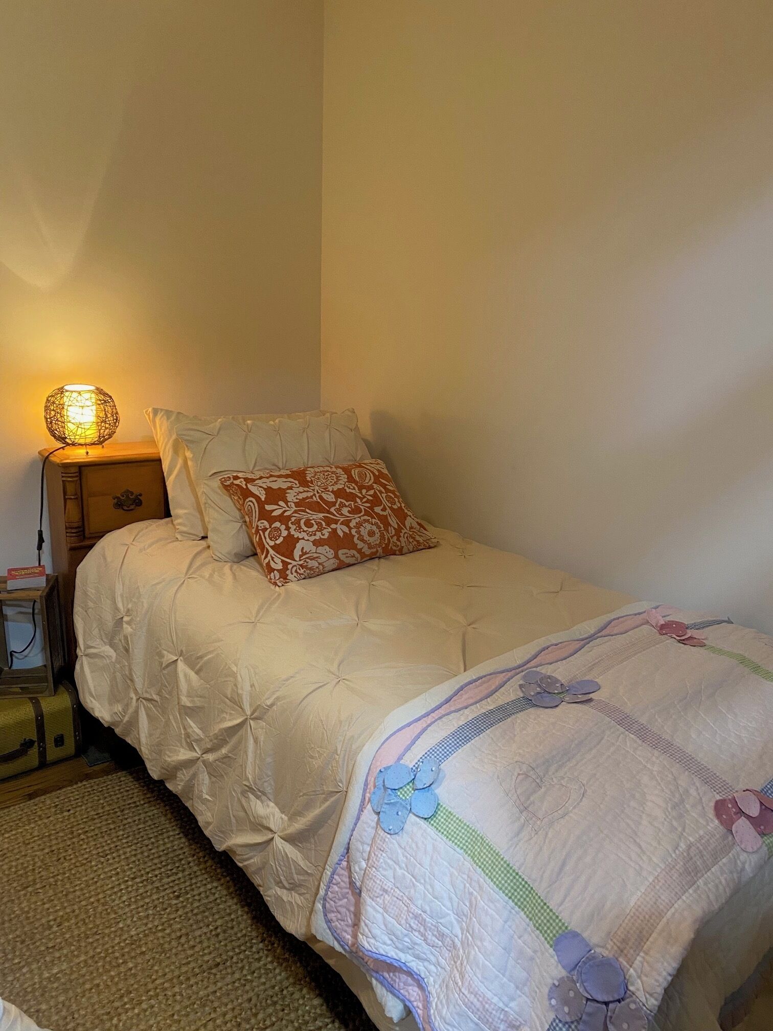 A neatly made bed with a floral pillow, a bedside lamp, and a suitcase on the floor.