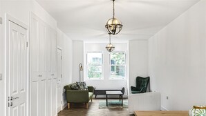Una habitación amplia con paredes blancas, suelo de madera tipo espiga, un sofá verde, un banco, una mesa de madera y un sillón verde.