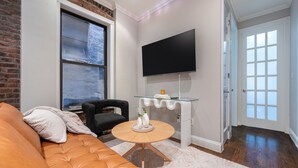 Ein Wohnzimmer mit Backsteinwand, großem Fenster, Flachbildfernseher, Glastisch und braunem Ledersofa.