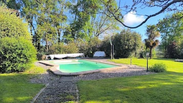 Un giardino con piscina, circondato da un prato curato e diversi alberi.