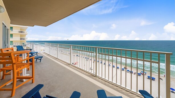 Een balkon met stoelen en tafels, uitzicht op het strand en een heldere lucht.