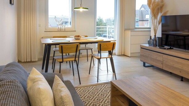 Een moderne woonkamer met een bank, een eettafel met stoelen, een houten bankje en een televisie op een houten kast.
