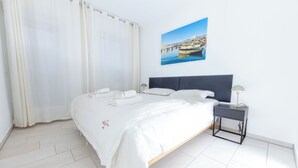 Een net opgemaakt bed met witte lakens, een hoofdbord en een nachtkastje met een lamp.